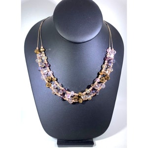 Puede incluir: Un collar de múltiples hilos con cadena de oro rosa y cuentas de vidrio iridiscente en tonos rosa, morado y marrón.