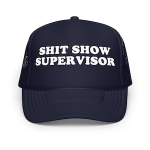 May include: Navy blue trucker hat with white text that reads "SHIT SHOW SUPERVISOR". The hat has a mesh back and a curved brim. A casual accessory for everyday wear.