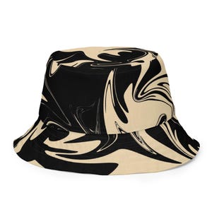 Puede incluir: Un sombrero de pescador con un llamativo diseño abstracto en negro y crema. El patrón del sombrero se asemeja a tinta arremolinada. Tiene un ala ancha y un estilo casual, adecuado para el uso diario.