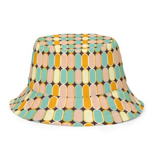 May include: A colorful bucket hat with a repeating pattern of vertical ovals in shades of teal, orange, pink, and cream against a dark brown background. The hat has a wide brim and a rounded crown.