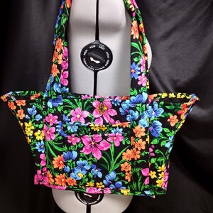 May include: A black quilted tote bag with a floral print featuring pink, blue, orange, and yellow flowers on a black background. The bag has two straps and a small pocket on the front.