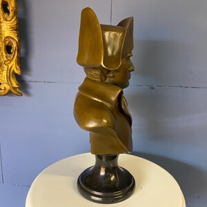 K&ouml;nnte beinhalten: Eine bronzene B&uuml;ste einer historischen Figur, die einen Mann mit Zweispitz und Milit&auml;rkleidung darstellt. Die Skulptur hat einen dunklen, polierten Sockel und steht vor einer blauen Wand. Die B&uuml;ste ist ein dekorativer Artikel.
