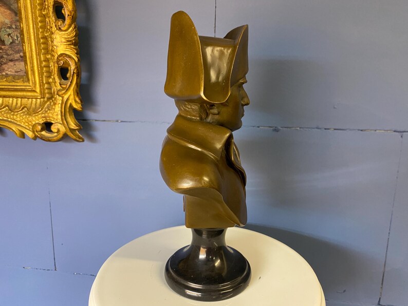K&ouml;nnte beinhalten: Eine bronzene B&uuml;ste einer historischen Figur, die einen Mann mit Zweispitz und Milit&auml;rkleidung darstellt. Die Skulptur hat einen dunklen, polierten Sockel und steht vor einer blauen Wand. Die B&uuml;ste ist ein dekorativer Artikel.