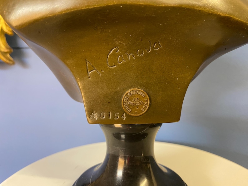 K&ouml;nnte beinhalten: Nahaufnahme einer Bronzeb&uuml;ste mit dunklem, poliertem Sockel. Die B&uuml;ste tr&auml;gt die Inschrift "A. Canova" und einen runden Stempel mit der Aufschrift "GARANTI J.B. DEPOSE PARIS". Die Nummer "46154" ist ebenfalls sichtbar.