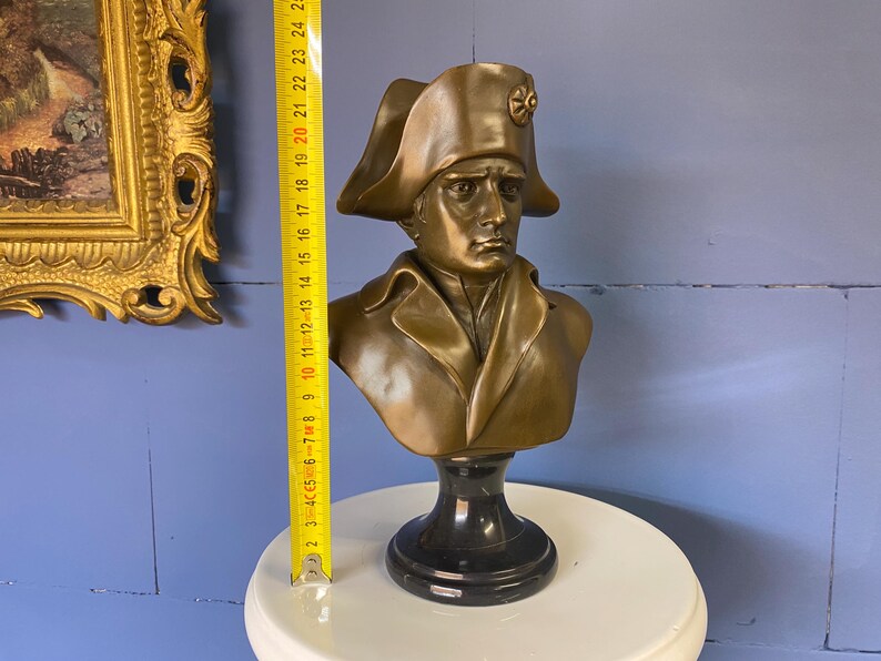 K&ouml;nnte beinhalten: Eine bronzefarbene B&uuml;ste einer historischen Figur, die einen Zweispitz und einen Milit&auml;rmantel tr&auml;gt. Die B&uuml;ste ist auf einem schwarzen Sockel montiert und ist etwa 25 cm hoch. Die B&uuml;ste steht auf einer wei&szlig;en Oberfl&auml;che, mit einem goldgerahmten Gem&auml;lde im Hintergrund.
