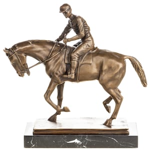 Könnte beinhalten: Eine Bronzeskulptur eines Jockeys auf einem Pferd. Der Jockey trägt eine Kappe und Reitkleidung. Das Pferd ist in Bewegung, die Beine ausgestreckt. Die Skulptur ist auf einem rechteckigen Marmorsockel montiert. Die vorherrschende Farbe ist Bronze.