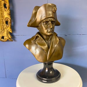 K&ouml;nnte beinhalten: Bronzefarbene B&uuml;ste einer historischen Figur, die einen Mann in einem Mantel und Hut im Milit&auml;rstil zeigt. Die Skulptur ist auf einem schwarzen Sockel montiert und zeigt einen klassischen Stil. Ein dekoratives Objekt.