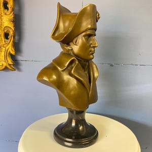 K&ouml;nnte beinhalten: Bronzefarbene B&uuml;ste einer historischen Figur, die einen Mann mit Zweispitz und Milit&auml;rmantel darstellt. Die B&uuml;ste ist auf einem schwarzen Marmorsockel montiert und zeigt ein klassisches Design.