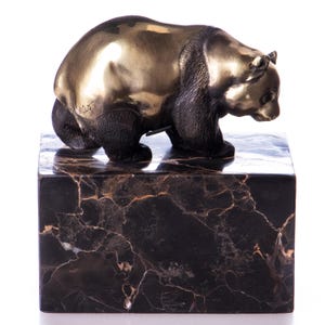 May include: A bronze bear sculpture with a polished finish, mounted on a black marble block. The bear is depicted in a walking pose, with detailed fur texture. The marble base has a dark, veined pattern.