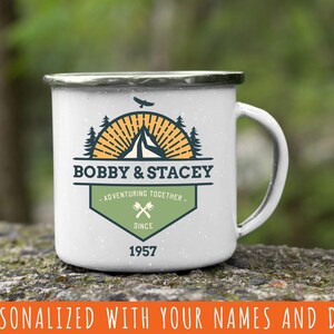 May include: White enamel camping mug with a black rim and handle. The mug features a custom design with the names "BOBBY & STACEY", a mountain, tent, and trees, and the text "ADVENTURING TOGETHER" and "SINCE 1957".