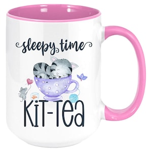 May include: White ceramic mug with a pink interior and handle. The mug features the text "sleepy time" and "Kit-Tea" with a watercolor illustration of a sleeping gray kitten in a teacup, a mouse, and a butterfly.