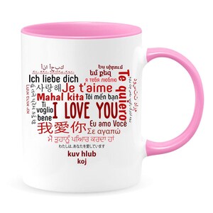 May include: White ceramic mug with a pink rim and handle. The mug features a red word cloud with the phrase "I Love You" in the center, surrounded by the words "I Love You" in various languages.
