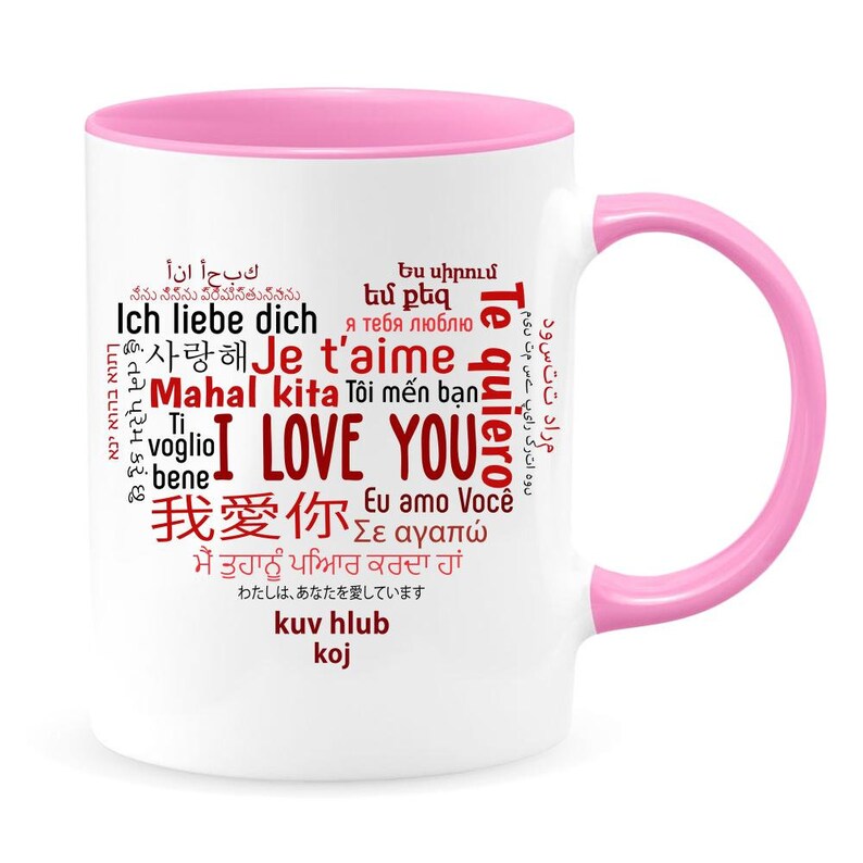 May include: White ceramic mug with a pink rim and handle. The mug features a red word cloud with the phrase "I Love You" in the center, surrounded by the words "I Love You" in various languages.