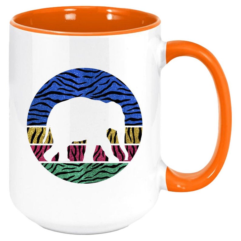 May include: White ceramic coffee mug with an orange rim and handle. The mug features a white silhouette of an elephant in a circle with a colourful zebra print background.