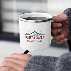 May include: White enamel camping mug with a black rim and handle. The mug has a vintage-inspired design with a mountain range graphic and the text "Adventuring Together Bobby & Stacey Since 1998".