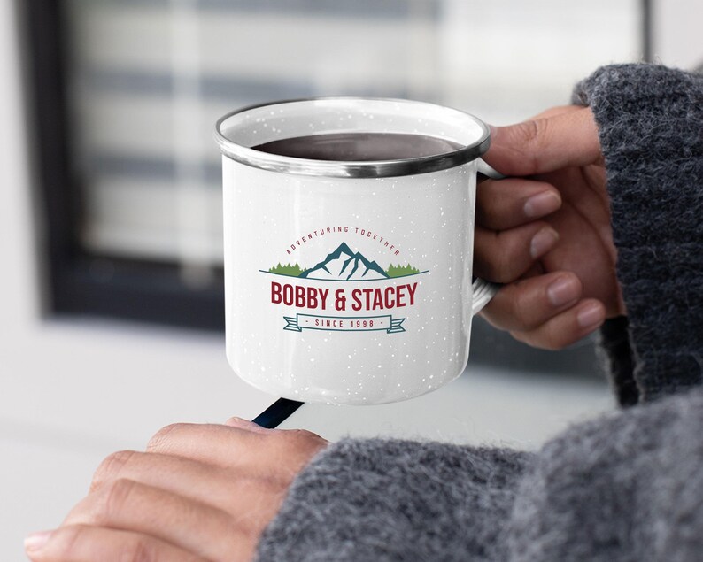 May include: White enamel camping mug with a black rim and handle. The mug has a vintage-inspired design with a mountain range graphic and the text "Adventuring Together Bobby & Stacey Since 1998".