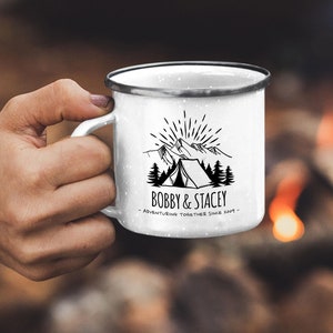 May include: White enamel camping mug with a black and white illustration of a tent, mountains, and trees. The text "BOBBY & STACEY - ADVENTURING TOGETHER SINCE 2009 -" is printed below the illustration.