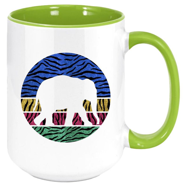 May include: White ceramic coffee mug with a green rim and handle. The mug features a white silhouette of an elephant against a colourful background of zebra stripes.