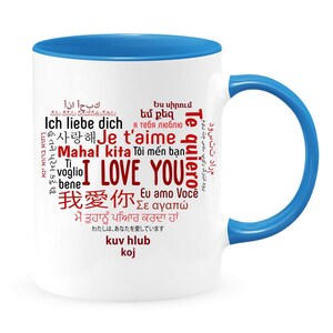 May include: White ceramic mug with a blue rim and handle. The mug features a red word cloud with the phrase "I Love You" in multiple languages.