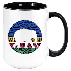 May include: White ceramic coffee mug with a black handle. The mug features a white silhouette of an elephant against a colourful background of blue, yellow, green, and pink zebra stripes.
