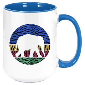 May include: White ceramic coffee mug with a blue rim and handle. The mug features a white silhouette of an elephant in a circle with a colourful zebra print background.