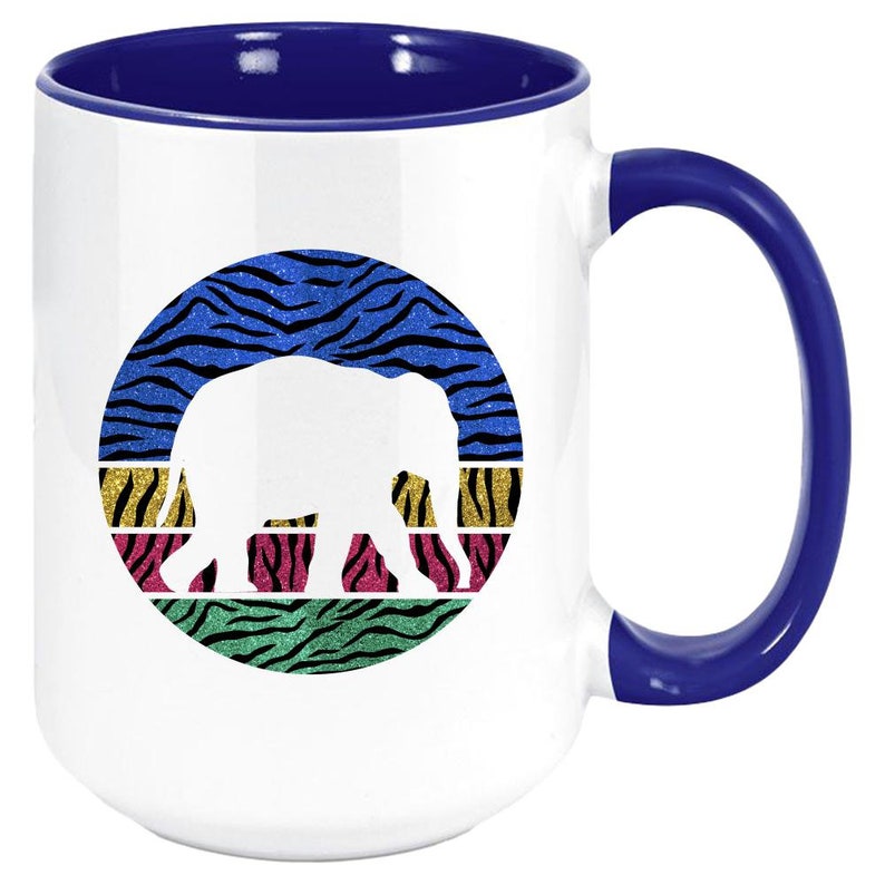 May include: White ceramic coffee mug with a blue rim and handle. The mug features a white silhouette of an elephant against a colourful background of blue, green, yellow, and pink zebra stripes.