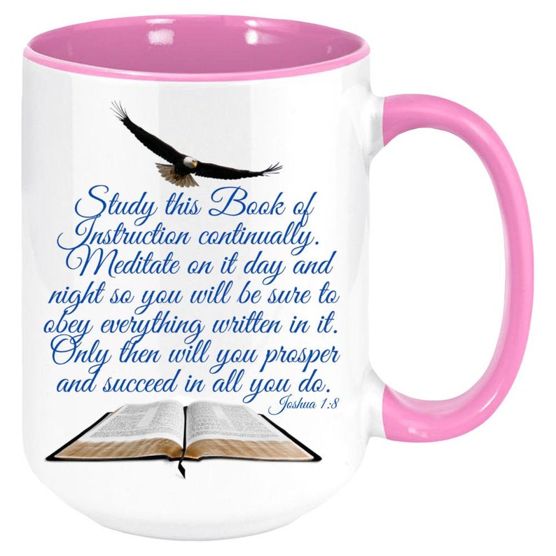 May include: White ceramic coffee mug with a pink rim and handle. The mug features a blue and white image of an open book with an eagle flying above it. The text on the mug reads "Study this Book of Instruction continually. Meditate on it day and night so you will be sure to obey everything written in it. Only then will you prosper and succeed in all you do. Joshua 1:8"