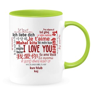 May include: White ceramic mug with a green rim and handle. The mug features a red word cloud with the phrase "I Love You" in multiple languages, including English, French, German, Spanish, Italian, Japanese, Korean, and Hindi.