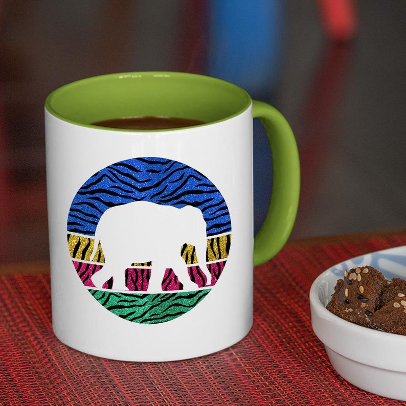 May include: White ceramic coffee mug with a green rim. The mug features a colourful graphic of a stylised elephant silhouette on a blue, green, pink and yellow striped background.