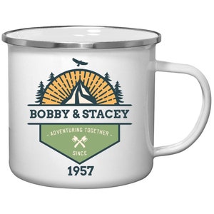 May include: White enamel camping mug with a silver rim and handle. The mug features a graphic with the text "BOBBY & STACEY" above "ADVENTURING TOGETHER SINCE 1957". The graphic includes a mountain, trees, and a bird.