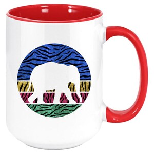 May include: White ceramic coffee mug with a red rim and handle. The mug features a white silhouette of an elephant in a circle with a colourful zebra print background.