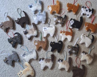 Könnte beinhalten: Eine Sammlung von vierundzwanzig nadelgefilzten Katzenornamenten in verschiedenen Farben und Mustern, darunter einfarbig schwarze, weiße, graue, braune, orangefarbene und mehrfarbige getigerte Designs. Jede Katzenfigur hat eine Schlaufe.