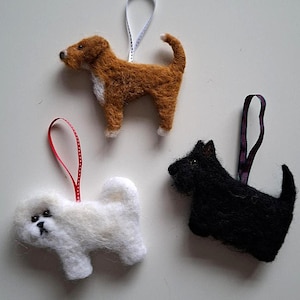 May include: Three felt dog ornaments. One is brown with white accents, another is white, and the third is black. Each has a ribbon loop for hanging. These handcrafted ornaments are perfect for dog lovers and add a touch of whimsy to any space.