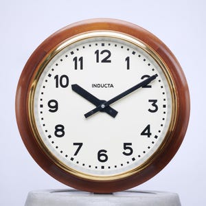 May include: A round, wooden-framed clock with a white face and black hands. The clock face has black numbers and the word "INDUCTA" printed in black at the top.
