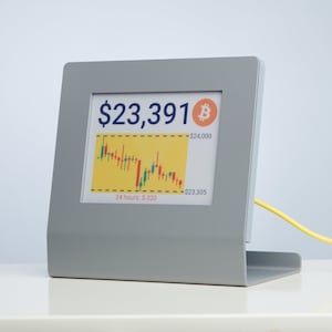 Puede incluir: Una pantalla digital gris con una pantalla blanca que muestra un precio de Bitcoin de $ 23.391. La pantalla también muestra un gráfico de líneas con barras verdes y rojas que representan las fluctuaciones de precios en las últimas 24 horas. El gráfico muestra un rango de $ 23.305 a $ 24.000.