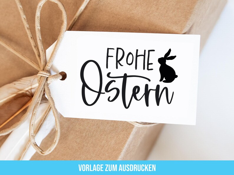 May include: A white gift tag with black text that reads "Frohe Ostern" with a black silhouette of a rabbit. The tag is tied to a brown package with twine.