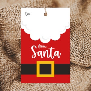May include: A rectangular gift tag with a Santa Claus design. The tag features a red background with a white cloud-like shape at the top and a black belt with a gold buckle. The words "from: Santa" are written in white script.