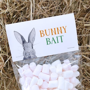 May include: A clear plastic bag filled with white and pink marshmallows. The bag has a white label with a drawing of a grey bunny and the text "BUNNY BAIT" in orange and green.