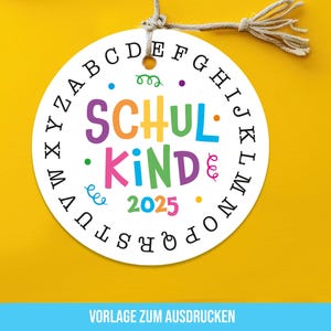 Puede incluir: Una etiqueta redonda blanca con las palabras "SCHUL KIND 2025" en letras coloridas. La etiqueta tiene un borde de letras y está suspendida por una cuerda sobre un fondo amarillo. El texto "VORLAGE ZUM AUSDRUCKEN" está en la parte inferior.