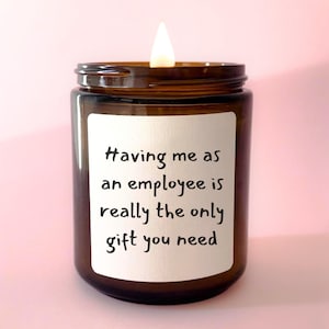 May include: A brown glass candle with a white label that reads "Having me as an employee is really the only gift you need". The candle is lit and the flame is visible.