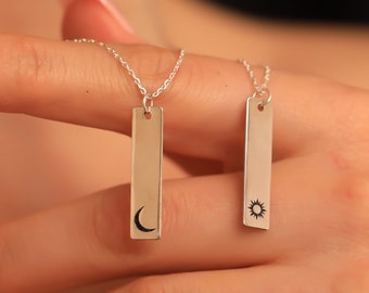 May include: Two silver necklaces with rectangular pendants. One pendant features a crescent moon design, and the other features a sun design.