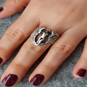 Close-up of silver-plated fantasy ring featuring a winged female figure, adjustable design, worn on hand.