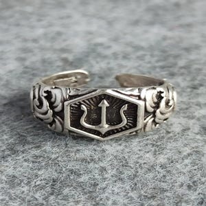 May include: Silver ring featuring a trident design within a hexagonal frame. The ring has a detailed floral pattern on the sides.