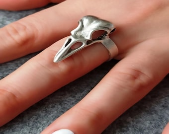 May include: A silver ring shaped like a bird skull. The ring is worn on a finger with white nail polish.