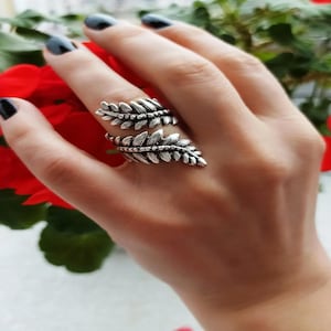 May include: A silver ring featuring a leaf design. The ring is adjustable and can be worn on any finger.