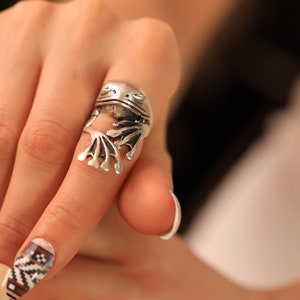 Könnte beinhalten: Ein silberner Froschring mit detaillierter Skulptur. Der Frosch sitzt auf einem Finger mit weißem Nagellack.