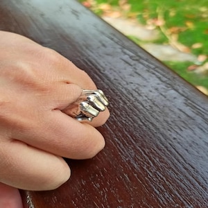 May include: A silver ring shaped like a clenched fist with five fingers.