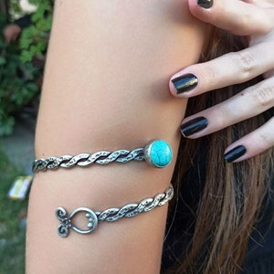 May include: A silver bracelet with a turquoise stone. The bracelet is made of twisted metal and has a decorative design.