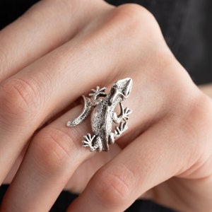 May include: A silver ring featuring a detailed, three-dimensional lizard design. The lizard is curled up with its tail wrapped around its body.