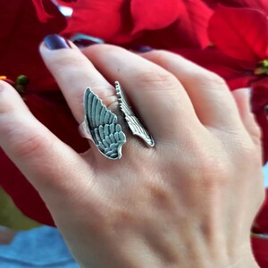 Può includere: Un anello d'argento con un designo ad ala dettagliato. L'anello è regolabile e può essere indossato su qualsiasi dito.